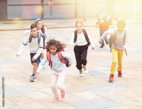 Team of positive schoolchildren running in race in the street and laughing outdoors