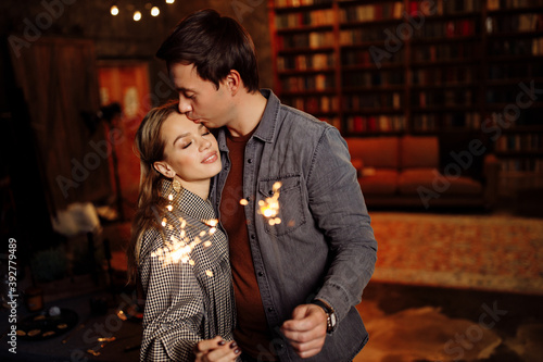 Beautiful couple hold sparklers in arms, adorable wife and charming husband enjoy festive mood, cozy winter holidays at home, New Year and Christmas celebration concept