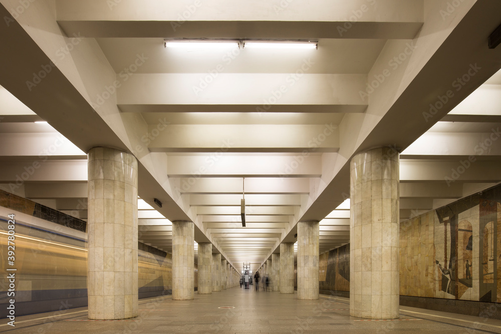 Linear perspective symmetrical view of an underground station with two rows of multiple columns and a blurred trace of a train going on the left. Silhouettes of people Linear perspective symmetrical view of an underground station with two rows of multiple columns and a blurred trace of a train going on the left. Silhouettes of people