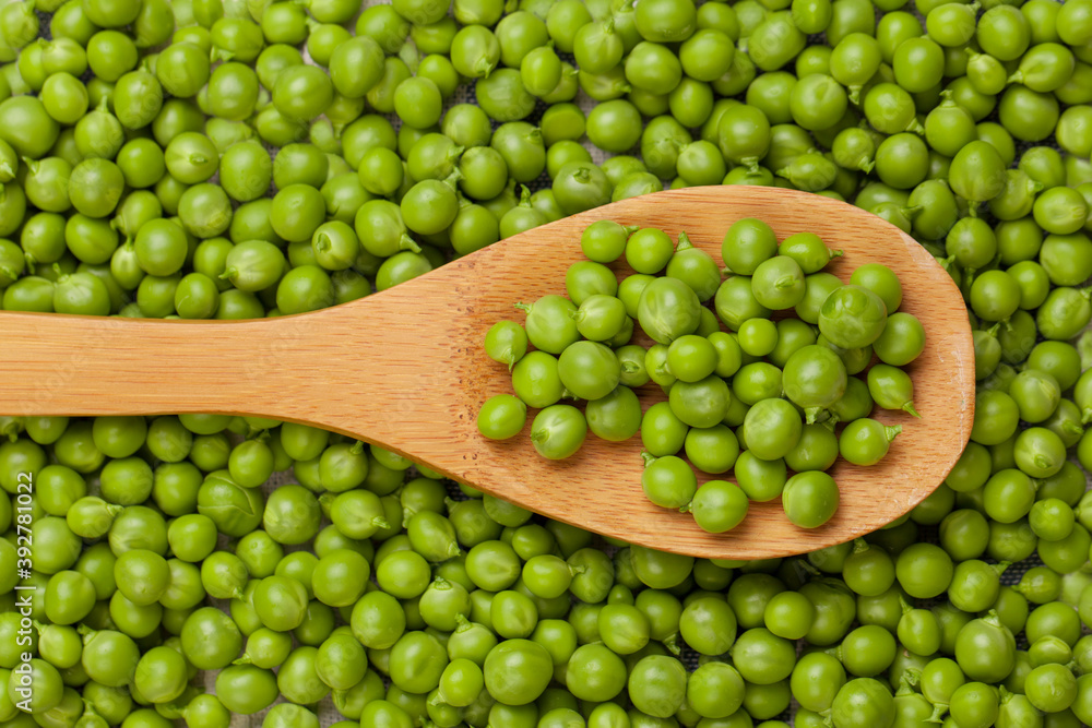 Wooden spoon with green peas on green peas background, top view