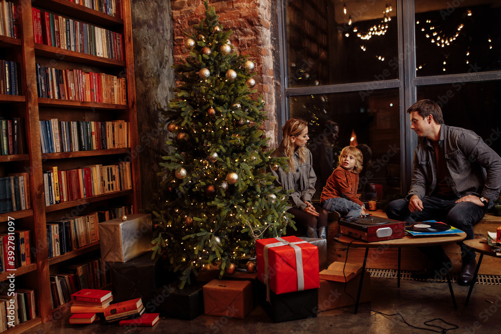 Lovely family sit near decorated Christmas tree with presents, enjoy festive mood, caring father with loving mother spend with preschooler son winter holidays, new year concept