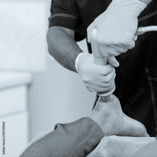 Dnepr, Ukraine- July 17, 2020: Patient getting non-surgical treatment with shock waves for plantar fasciitis. black and white image with blue tint to emphasize the concept of high technology