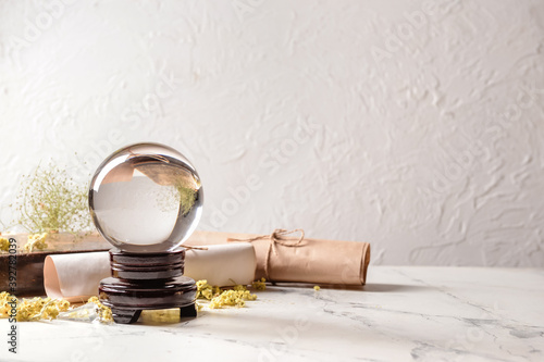 Crystal ball of fortune teller, spell book and scrolls on table photo