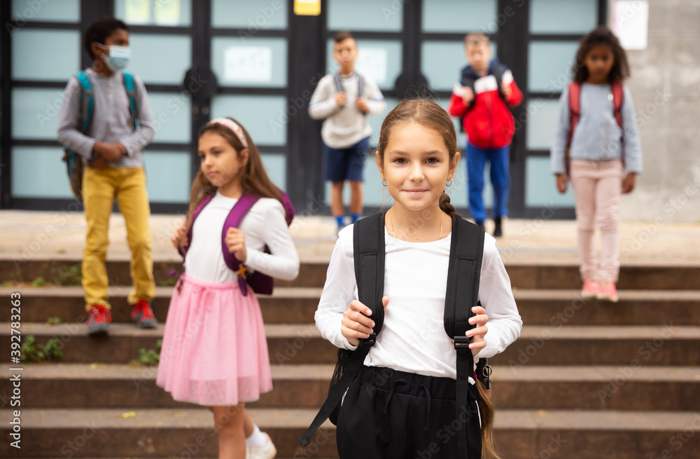 Attractive teenage girl carrying backpack on her shoulders, walking outdoors on autumn day, going to school.