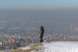 Photographer takes pictures while standing on the hill. Background - urban landscape in the fog. Winter, white snow. Blur.