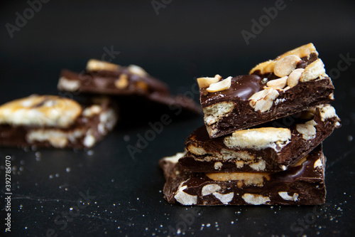Close-up of dark chocolate with cracker cookies and cashews, against a dark background with blur in the background.
