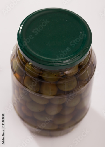 Glass jar of green unpitted olives in brine on white background.. photo