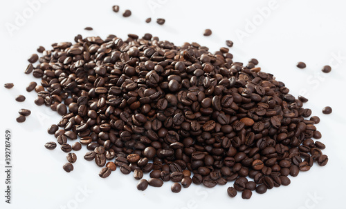 Pile of aromatic roasted coffee beans on white surface..
