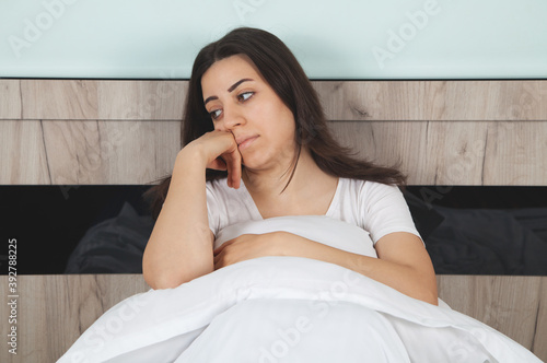 Upset sad woman suffering from in bed. Woman sitting on a bed looking sad.