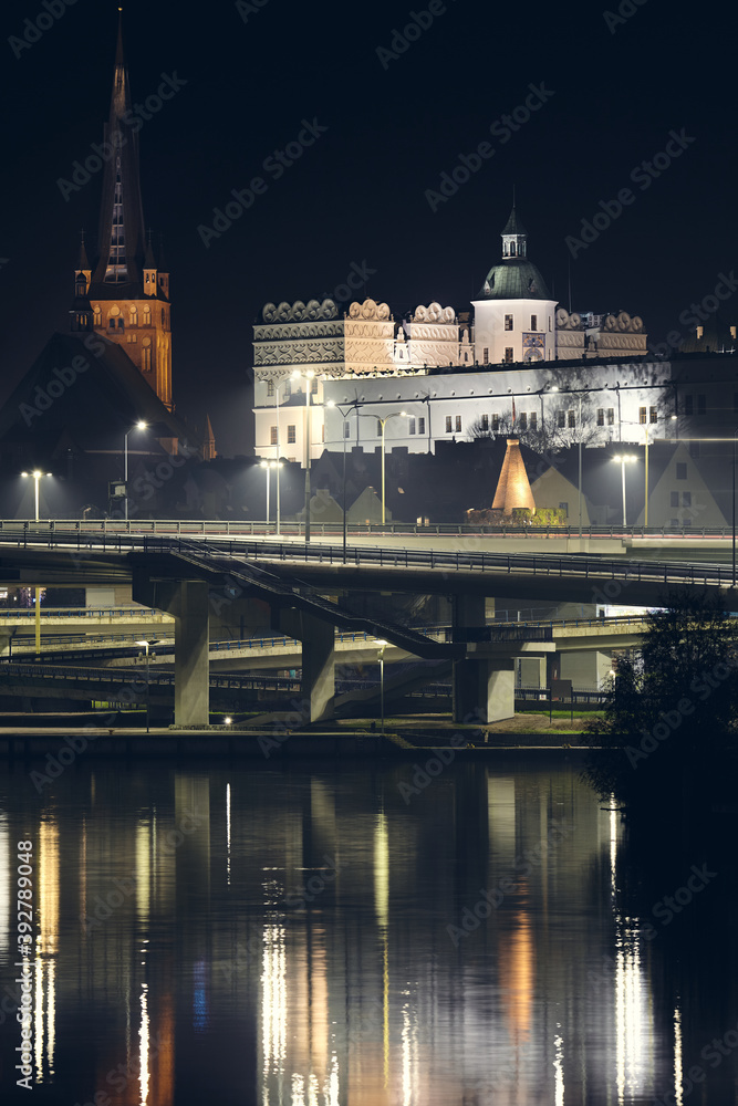 The Ducal Castle (Zamek Ksiazat Pomorskich) and Cathedral in Szczecin reflected in Odra River at foggy night, Poland.