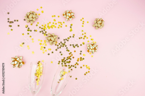 Golden bows and confetti stars with glasses lie on a pink background. Copy space