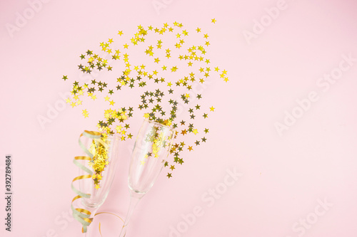Golden bows and confetti stars with glasses lie on a pink background. Copy space