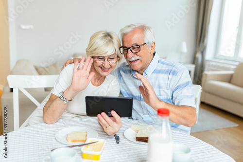 Senior couple is talking online via video connection on tablet. Having nice time withfriends and family via video call.Holding their hands together photo