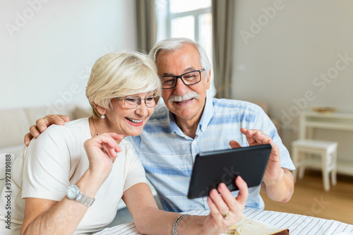 Happy old family couple talking with grandchildren using tablet , surprised excited senior woman looking at tablet waving and smiling.