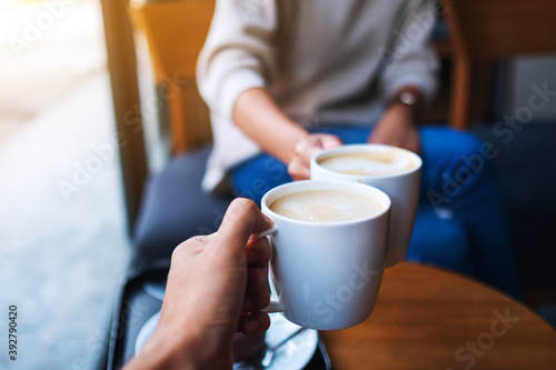 Closeup image of man and woman clinking white coffee mugs in cafe