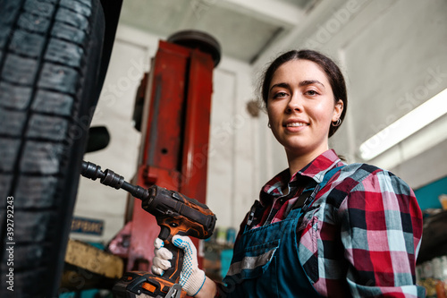 Portrait of a young Caucasian female mechanic, in uniform, poses with a wrench in her hands and smiles. Bottom view. Indoors garage