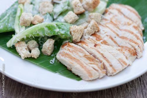 Grilled chicken breast Caesar salad in white plate on wooden table at the restaurant.