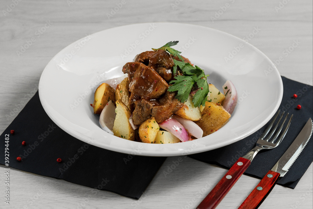 Stewed lamb fillet with new potatoes and red onion is on the wooden background with fork and knife. Stewed lamb fillet with new potatoes and red onion is on the wooden background with fork and knife.
