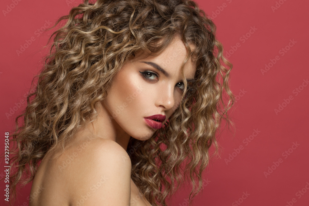 Fashion portrait of nice young woman with makeup and curly hairstyle on red background