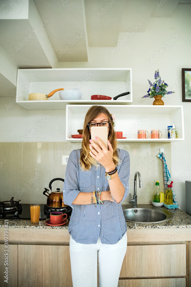 Modern young woman using cellphone in the kitchen.
