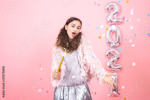 Young woman on a pink background with silver ballons in the form of the numbers 2021