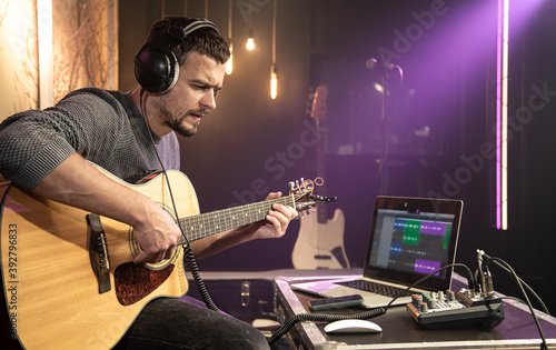 European man plays the guitar while recording a track in a music studio.
