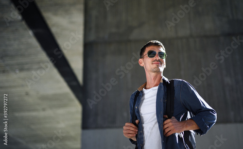 Low-angle view of young attractive man with backpack standing outdoors in city.
