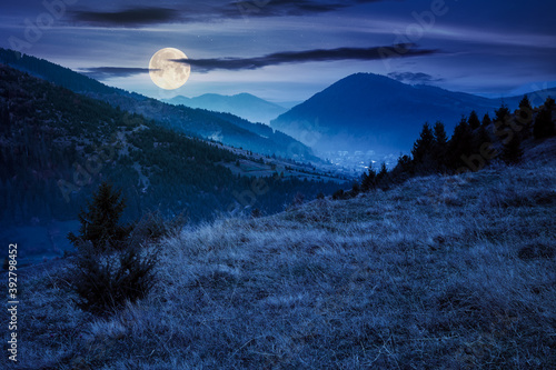 foggy morning in carpathian countryside at night. village down in the rural valley. trees in fall foliage on the hills in full moon light. gloomy weather