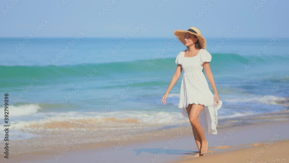 Young woman in white dress and hat walks barefoot on seashore. Slow motion Young woman in white dress and hat walks barefoot on seashore. Slow motion