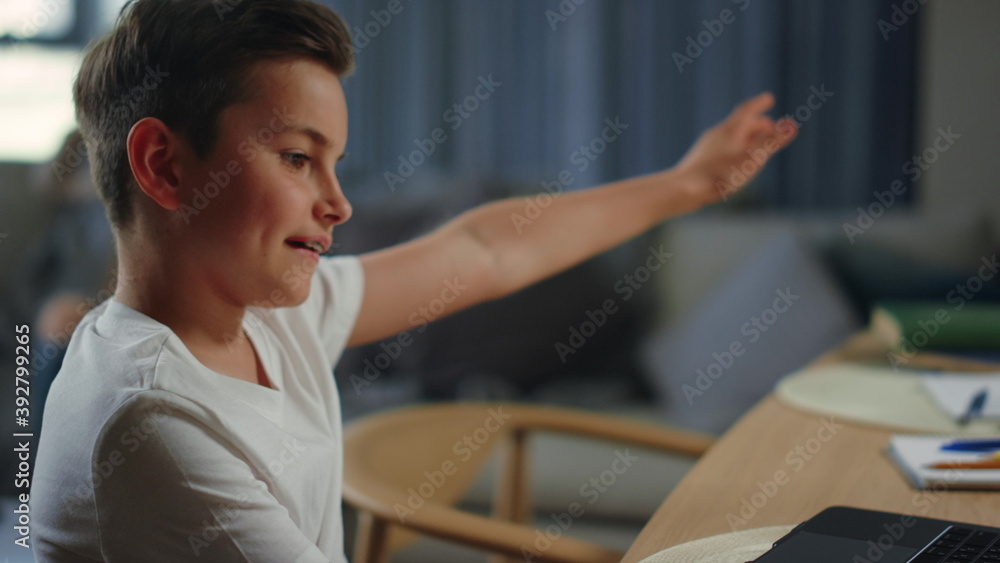 Active kid studying home. Cool boy rising hand during video class on laptop. Active kid studying home. Cool boy rising hand during video class on laptop.