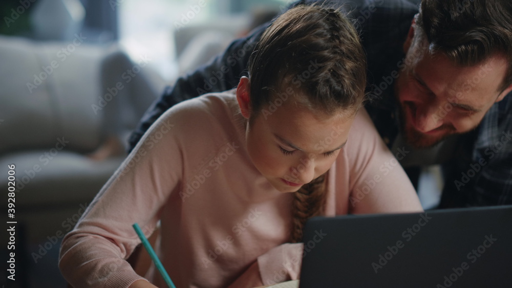Daughter studying remotely under father supervision. Girl writing notebook. Daughter studying remotely under father supervision. Girl writing notebook.