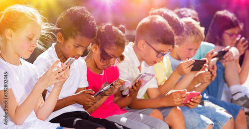 Happy children using mobile devices outdoors at sunny day