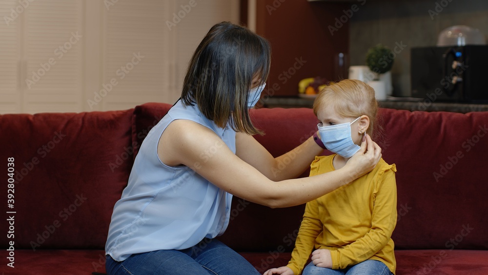 Mother puts on little sick daughter medical mask. Stay home. Coronavirus or COVID-19 pandemic disease symptoms. Child girl and woman on quarantine lockdown. Mom teaching kid to put on a medical mask Mother puts on little sick daughter medical mask. Stay home. Coronavirus or COVID-19 pandemic disease symptoms. Child girl and woman on quarantine lockdown. Mom teaching kid to put on a medical mask