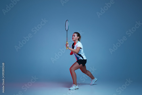 Beautiful handicap woman practicing in badminton isolated on blue background in neon light. Lifestyle of inclusive people, diversity and equility. Sport, activity and movement. Copyspace for ad.