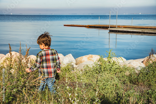 A child at the seaside discovering the beauty of nature gaining eagerness, learning life and feeding his curiosity. A kid or toddler by the sea exploring nature bears childhood and interest concept photo