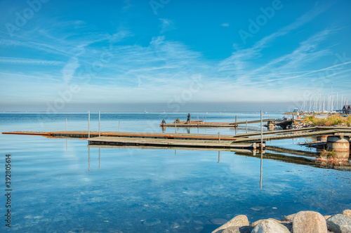 Wallpaper Mural People relax on a wooden jetty as the sun is warm, the water is crystal clear conveying a vacation break, rest and holiday concept. Tranquil people lie on a pier by a calm Baltic sea taking a photo Torontodigital.ca