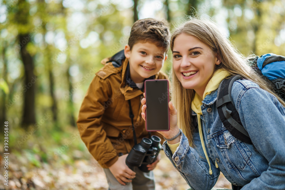 Happy mother and son are hiking in forest. They are using maps on smart phone. There is copy space on phone screen. Happy mother and son are hiking in forest. They are using maps on smart phone. There is copy space on phone screen.