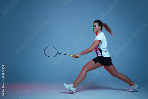 On the run. Beautiful handicap woman practicing in badminton isolated on blue background in neon light. Lifestyle of inclusive people, diversity and equility. Sport, activity and movement. Copyspace.