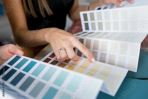 Close-up of two women choosing samples of wall paint. Interior designer consulting a client looking at a color swatch. House renovation concept photo