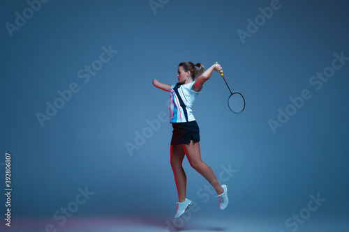 In jump. Beautiful handicap woman practicing in badminton isolated on blue background in neon light. Lifestyle of inclusive people, diversity and equility. Sport, activity and movement. Copyspace.