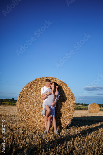 Attractive woman posing in the mown wheat fields with a sheaf in the village. Hay bales on the field after harvest, a place for a photo session of a beautiful Slavic couple