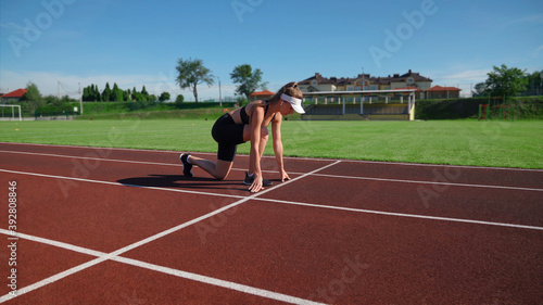 Woman practicing sprinter position at stadium.