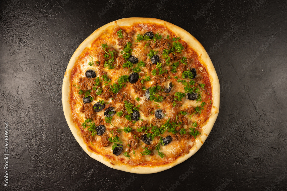 Round hot freshly baked pizza with tuna, olives, dill and cheese lies on a black stone kitchen table
