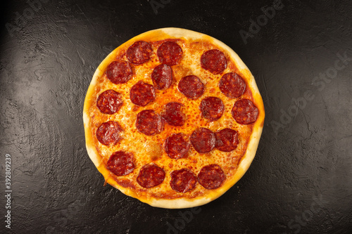 Round hot freshly baked pizza with salami and cheese lies on a black stone kitchen table