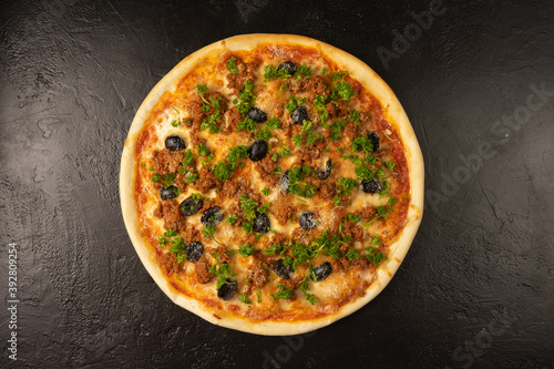 Round hot freshly baked pizza with tuna, olives, dill and cheese lies on a black stone kitchen table