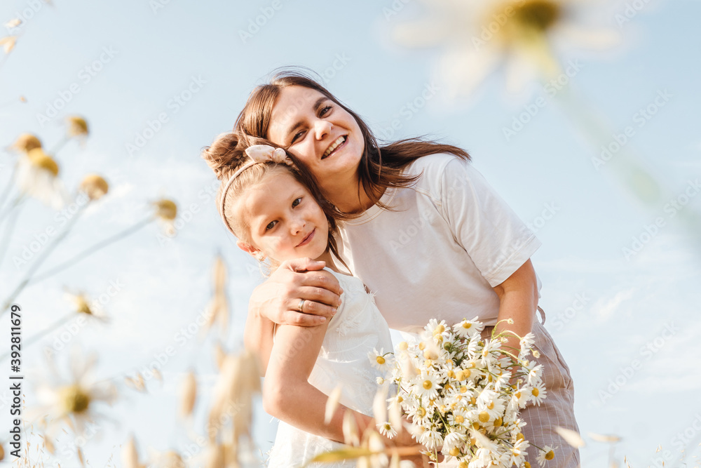 Beautiful young mother and her daughter having fun at the field. Chamomile on foreground, sky background. White clothes. Beautiful young mother and her daughter having fun at the field. Chamomile on foreground, sky background. White clothes.