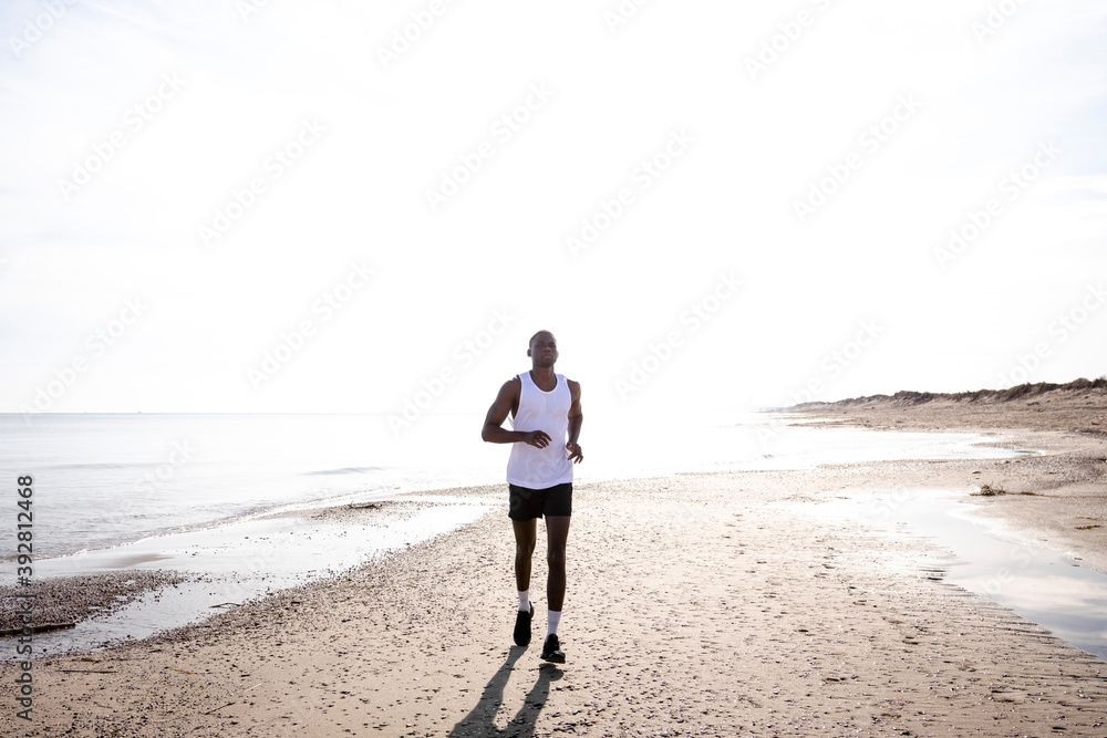 Black young man is jogging on street among the sun shines back light.