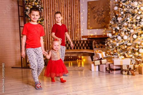 two brothers and a little sister holding hands in full height for Christmas. three happy children at Christmas photo shoot