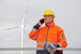 Engineer with protective work wear talking on mobile phone in front of a wind turbine