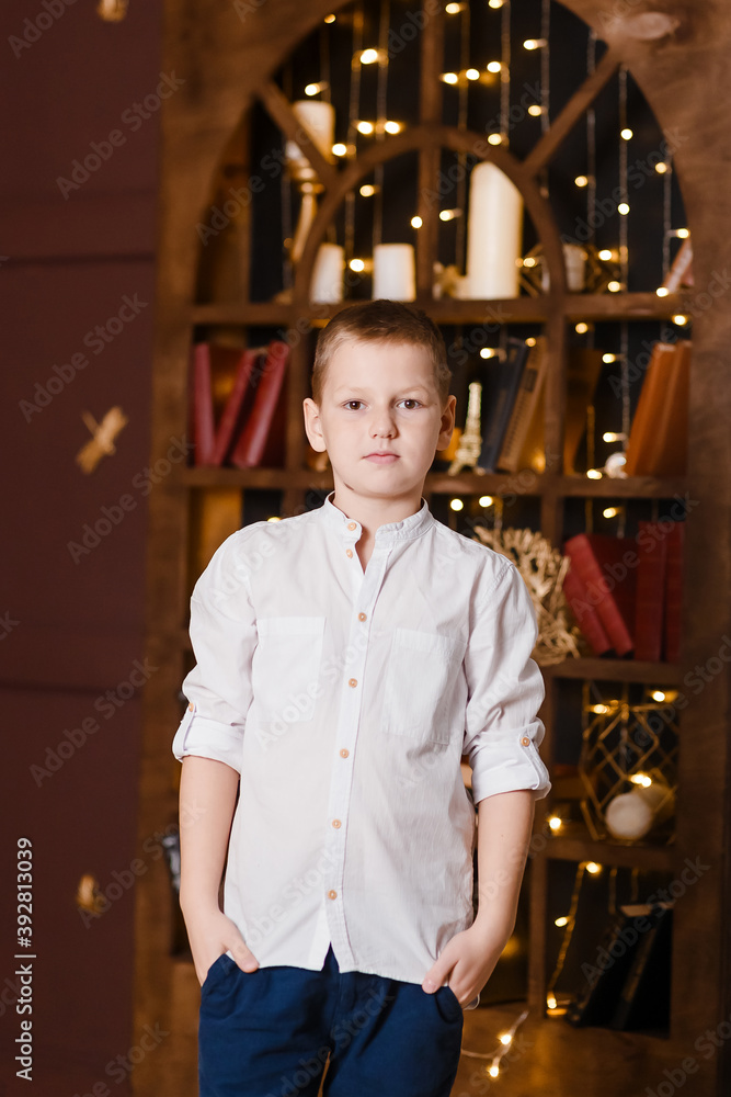 nine-year-old boy in a white shirt looks at the camera in a dark room. Handsome
